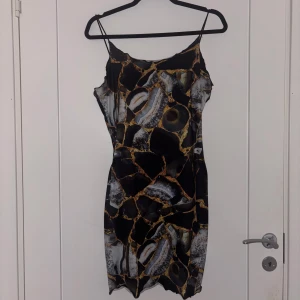 Svart mönstrad kort klänning - Cool kort klänning med smala axelband och abstrakt mönster i svart, grått och beige. Figurnära passform och stretchigt material, perfekt för en trendig look. Klänningen har en modern vibe och passar dig som gillar att sticka ut.