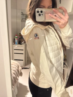 Vit pufferjacka från PJS med huva - Säljer en snygg vit pufferjacka från Parajumpers med quiltad framsida och huva. Jackan har dragkedja och logotyp på vänster axel. Jackan är i storlek L men passar S uppåt