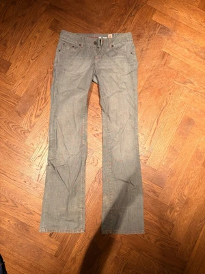 Grå raka jeans från Levi's - Säljer ett par grå jeans från Levi's med raka ben och klassisk femficksdesign. Jeansen har låg midja och subtila sömmar, samt Levi's ikoniska röda etikett på bakfickan. Perfekta för en avslappnad och stilren look.