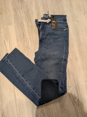 Mörkblå skinny jeans från ONLY - Snygga mörkblå skinny jeans från ONLY med klassisk femficksdesign och hög midja. Jeansen har en smal passform och är tillverkade i stretchigt denimtyg för extra komfort. Perfekta för en trendig och avslappnad look.