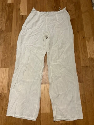 Vita vida byxor i tunt material - Säljer ett par vita byxor i med avslappnad passform och dragsko i midjan. Byxorna är tillverkade i tunt och luftigt ematerial, perfekta för en chill och stilren look. Passar dig som gillar bekväma och svala plagg med loose fit.