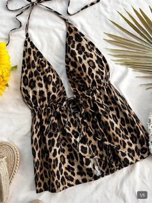 Leopardmönstrad halterneck linnetopp - Snygg leopardmönstrad linnetopp med halterneck och knyt i ryggen. Toppen har djup v-ringning och är tillverkad i ett lätt, glansigt material som känns skönt mot huden. Perfekt för dig som vill sticka ut med en trendig look.