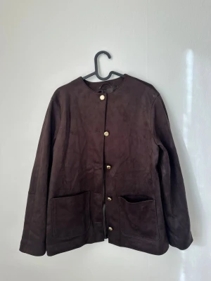 Mörkbrun jacka i mockaimitation  - Stilren mörkbrun cardiganjacka i mjuk mockaimitation med rund halsringning och dekorativa guldknappar framtill. Aldrig använd 