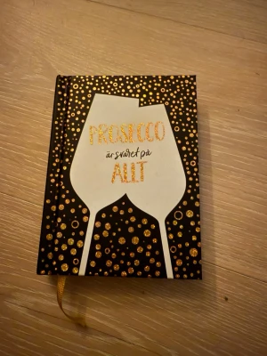 Prosecco är svaret på allt bok - En snygg bok med svart omslag dekorerat med guldiga prickar och två vita glas. Texten 'Prosecco är svaret på allt' står i glittrande guld. Perfekt som present eller till dig som älskar prosecco och humor.