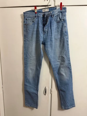 Ljusblå jeans från Pull&Bear - Säljer ett par ljusblå jeans från Pull&Bear med klassisk femficksdesign och knäppning med knappar. Jeansen har en rak passform och är tillverkade i bomullsdenim. Perfekta för en avslappnad och trendig look.