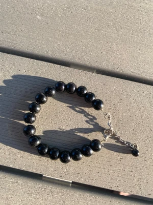 Svart pärlarmband med silverkedja - Snyggt egentillverkat armband med svarta, glansiga pärlor och justerbar silverfärgad kedja.. Pärlorna är runda och sitter tätt på rad, vilket ger ett klassiskt intryck. Längd ca 15 cm
