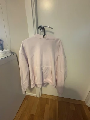 Ljusrosa hoodie från 157 - Mjuk och skön ljusrosa hoodie från 157 med klassisk känguruficka framtill och huva. Tillverkad i ett bomullsliknande material som känns bekvämt mot huden. Perfekt för en avslappnad och chill stil.