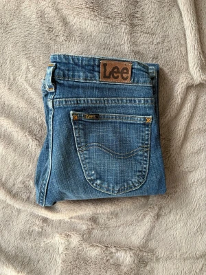 Vintage jeans - PRIS GÅR ATT DISKUTERA. Snygga blå vintage jeans från Lee med klassisk bootcut-modell och tydliga kontrastsömmar. Jeansen har bakficka med Lee-logga och är tillverkade i slitstark denim. Perfekta för dig som gillar en tidlös och avslappnad stil. Köpta mellan 1985-2005 så därav går dom inte längre att få tag på💗Midjemått: 37/38cm, Innerbenslängd: 76cm, Lårmått: 20cm