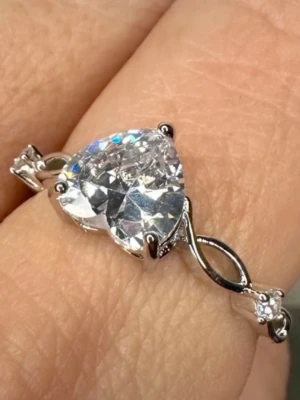 Ny romantisk ring med strassgnistrande hjärta Justerbar Storlek Nickelfri  - Romantisk hjärtformad ring i silverfärgad metall med stor klar facetterad sten och små dekorativa sidostenar. Fångar ljuset vackert och ger ett gnistrande, elegant uttryck. Perfekt som nätt statement- eller cocktailring och lätt att matcha till både vardag och fest. Justerbar storlek som passar flera fingrar.  Mått: hjärtsten ca 1 cm Material: silverfärgad metall, klar glassten Skick: ny utan prislapp, oanvänd