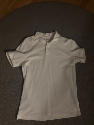 Vit pikétröja i bomull - Klassisk vit pikétröja med krage och korta ärmar. Tröjan har knappar vid halsen och är gjord i mjuk bomull, perfekt för en clean och enkel stil. Denna fina piké är bara använd en enda gång då jag växte ur den snabbt. Skulle rekommenderas för någon som är emellan 175-185 cm, sitter som vanlig medium helt enkelt. Skriv om du har frågor och vill du ha en svart så finns det i min profil också 