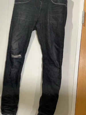 dondup  - Säljer ett par svarta skinny jeans med slitning på vänster knä och klassisk femficksdesign. Jeansen har en tight passform och är tillverkade i denim med stretch för extra komfort. Perfekta för en trendig och avslappnad stil.