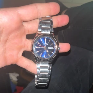 Seiko klocka med blå urtavla - Stilren casio klocka med metallarmband och en snygg blå urtavla. Klockan har dag- och datumvisning samt silverfärgade detaljer på urtavlan. Perfekt accessoar för dig som gillar klassisk design med modern touch.