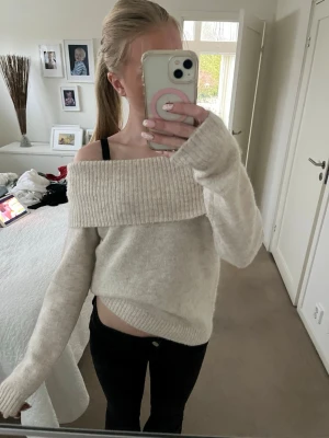 Off shoulder stickad tröja beige - Mysig stickad tröja i beige med bred ribbad off shoulder-krage. Tröjan har långa ärmar och en avslappnad passform som ger en cool och trendig look. Perfekt att styla med jeans eller kjol för en casual vibe.