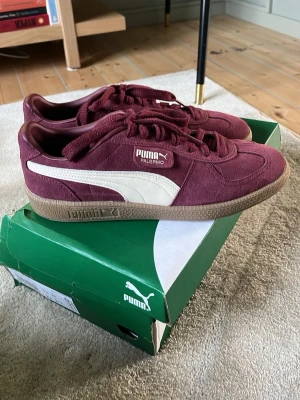 Vinröda Puma Palermo sneakers - Snygga vinröda Puma Palermo sneakers i mocka med klassisk vit sidostrip och gummisula. Skorna har lågt skaft och matchande vinröda skosnören. Perfekta för dig som gillar retrostil och streetwear.