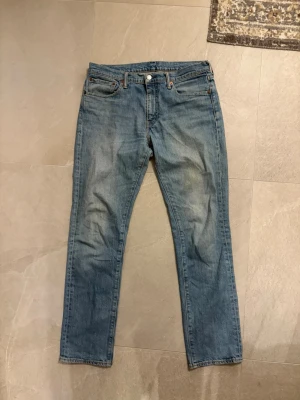 Blå Levi’s 511 jeans med klassisk passform - Ett par blå jeans med rak passform och fem fickor. Jeansen har en klassisk look med ljus tvätt och subtila slitningar. Tillverkade i denim med bälteshällor och knappgylf. Perfekta för en avslappnad stil.