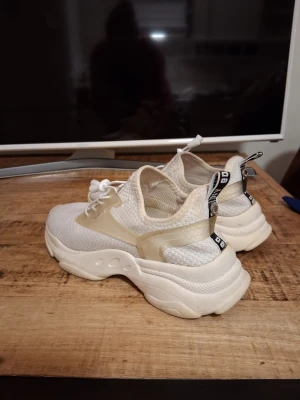 Skor - Steve Madden  - Snygga vita sneakers med chunky sula och ovandel i mesh. Skorna har transparenta detaljer på sidorna och svartvit dragflik bak. Perfekta för en trendig streetstyle-look.