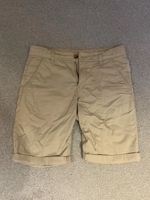 Beige shorts - Snygga beige shorts från Åhlénsmed klassisk passform. De har uppvikta benslut, sidofickor och bakfickor. Perfekta för varma dagar och enkla att matcha med olika outfits. Passar i upp till 175cm