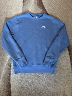 Blå sweatshirt från Nike - Snygg blå sweatshirt från Nike med klassisk rund halsringning och vit Nike-logga broderad på bröstet. Tröjan har ribbade muddar vid ärmslut och nederkant, perfekt för en avslappnad och sportig stil.