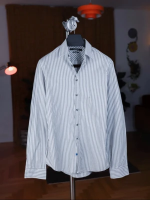 Randig skjorta från Tiger of Sweden - Snygg vit och grå randig skjorta från Tiger of Sweden. Skjortan har klassisk krage, knäppning framtill och lång ärm. Slim fit-modell som ger en modern och stilren look. Perfekt för dig som gillar stilrena plagg med lite edge.