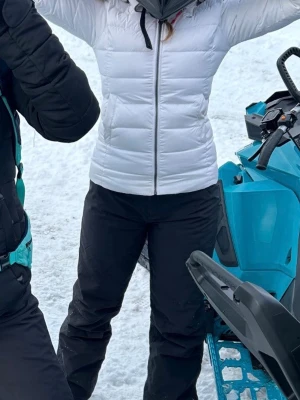 Vit dunjacka med dragkedja - Snygg vit dunjacka med figurnära passform och dragkedja framtill. Jackan har en hög krage med pälsluva och quiltad design som håller värmen under kalla dagar. Perfekt för vinterns alla äventyr.