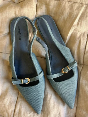 Blå denim slingbacks - Snygga ballerinaskor / slingbacks i blå denim från Stephan med spetsig tå och öppen häl. Skorna har en smal rem med guldfärgat spänne över foten och en bekväm sula så lätt att gå i. Passar 39-41