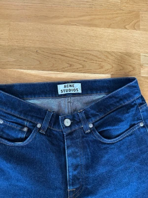 Mörkblå jeans från Acne Studios Rock New Raw - Snygga mörkblå jeans från Acne Studios med klassisk femficksmodell och raka ben. Jeansen har silverfärgade knappar och detaljer samt en hög midja. Slim fit