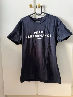 Peak Performance t-shirt - Snygg svart t-shirt från Peak Performance med vit logga tryckt på bröstet. Klassisk rund halsringning och korta ärmar. Perfekt för en avslappnad och sportig stil.