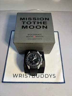 Omega x Swatch MoonSwatch svart - Snygg Omega x Swatch MoonSwatch Mission to the Moon med svart urtavla, vita detaljer och svart biokeramiskt armband. Klockan har kronograf och tydliga index, inspirerad av klassiska Speedmaster. Levereras med originalbox, extra band och certifikat. Det extra gummibandet är ifrån wristbuddy, klockan är köpt 2022 men bytte batteriet här om dagen. Det sitter även ett skyddsplast vilket gör att det inte är en enda repa under plasten på ”glaset”. Det går att köpa klockan utan gummibandet