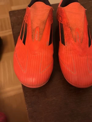 Adidas F50 röda fotbollsskor - Säljer ett par röda Adidas F50 fotbollsskor med svarta detaljer och stilrena linjer. Skorna har en strömlinjeformad design utan snörning och ovandel i syntetmaterial för bra bollkontroll. Perfekta för dig som vill sticka ut på planen har använts i en månad och skulle säga att de är bra skick 