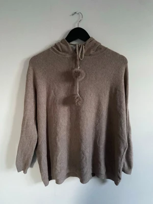 Beige hoodie med pälstofsar och nitar - Mysig beige hoodie med luva och pälstofsar på snörena. Luvan är dekorerad med små guldfärgade nitar. Den är finstickad och gjord av bomull. Det går även att ta bort pälstofsarna ifall man vill det🥰😊. 
