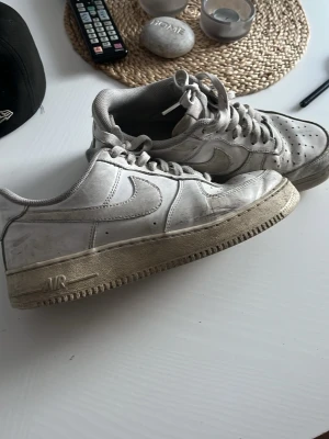 Vita Nike Air Force 1 låga sneakers - Klassiska vita Nike Air Force 1 sneakers i lågt utförande. Skorna har en ikonisk siluett med perforerad tå, vita skosnören och tydlig swoosh på sidan. Tillverkade i läder med gummisula och diskreta detaljer. Perfekta för en streetwear-look.