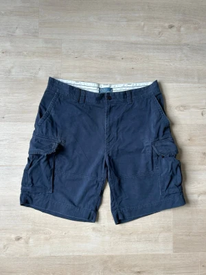 Blåa Ralph Lauren Cargoshorts Shorts Storlek W40 - Mycket fina Ralph Lauren shorts i blå färg | Jeansen är i mycket bra skick och sparsamt använda. |  Äkta som allt annat jag säljer! ✅ |  Storlek: W40 | Skick: Mycket Bra Skick | Färg: Blå | Märke: Ralph Lauren | Modell: Shorts |   Hör gärna av dig vid frågor så svarar jag så fort jag kan! 😁 |  (SKU - 174)