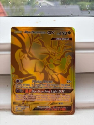 Ultra Necrozma GX Pokémonkort - Säljer ett Ultra Necrozma GX samlarkort från Pokémon. Kortet har en guldfärgad, holografisk yta med motiv av Ultra Necrozma och text på engelska. Perfekt för dig som gillar att samla eller spela Pokémonkort.