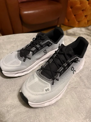 Gråa On cloud sneakers - Snygga sneakers från On Cloud i grått och svart med vit sula. Ovandelen är i meshmaterial för bra andningsförmåga och skorna har svarta snören och detaljer. Perfekta för dig som gillar stilrena och sportiga skor.
