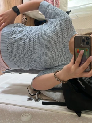Ljusblå stickad topp med kort ärm - Säljer en ljusblå stickad topp med korta ärmar och rund hals. Tröjan har ett snyggt hålmönster och ribbade kanter vid ärmslut och nederkant. Perfekt för dig som gillar en fräsch och stilren look.