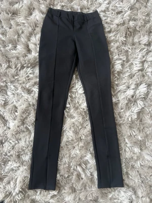 Svarta kostymbyxor med dragkedja - Snygga svarta kostymbyxor med dragkedja nedtill, figurnära look. Passar perfekt till ett par boots eller öppna klackar. 