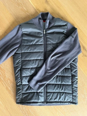 Grå quiltad cardigan från Iceland - Snygg grå cardiganjacka från Iceland med quiltad front och stickade ärmar. Jackan är i storlek M men skulle säga att den är mer S än M. Köpt i Köpenhamn för ungefär ett halvår sedan och har inte använt den mycket alls.