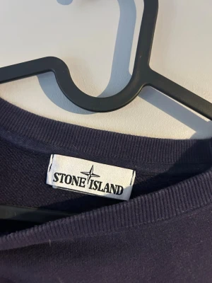 Mörkblå sweatshirt från Stone Island - Mörkblå sweatshirt från Stone Island med klassisk rund halsringning och ikonisk avtagbar patch med logga på vänster ärm. Tröjan har en avslappnad passform och är tillverkad i mjuk bomull. Perfekt för en stilren och trendig look.