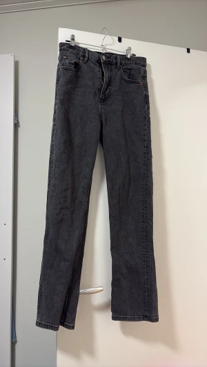 Svarta raka jeans med hög midja - Säljer ett par svarta raka jeans med hög midja och klassisk femficksmodell. Jeansen har en enkel design utan slitningar och är tillverkade i kraftig denim. Perfekta för dig som gillar en clean och tidlös look.