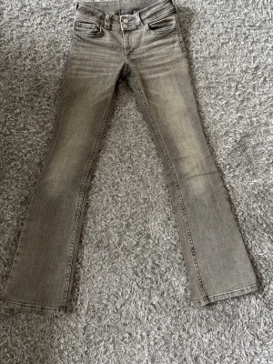 Grå bootcut jeans från H&M - Snygga grå bootcut jeans från H&M med justerbar midja och låg midja. Jeansen har klassisk femficksdesign och cool tvättad look. Perfekta för dig som gillar en avslappnad men trendig stil.
