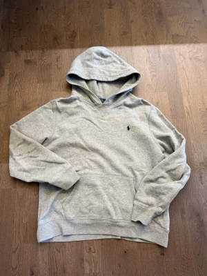 Grå hoodie från Polo Ralph Lauren - Snygg grå hoodie från Polo Ralph Lauren med klassisk huva och känguruficka. Tröjan har det ikoniska lilla broderade logotypen på bröstet och är gjord i mjuk bomullsblandning. Perfekt för en avslappnad och stilren look.
