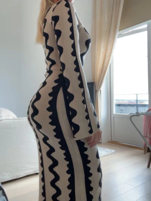 Beige långklänning från NA-KD - Långklänning i beige med svarta vågiga ränder. Klänningen har långärmad design och figurnära passform som framhäver siluetten. Materialet är stickat och känns mjukt mot huden. Sparsamt använd. Kostar 800 på NA-KDs hemsida 🩷