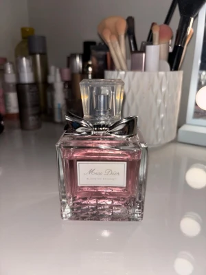 Miss Dior Blooming Bouquet parfym - Miss Dior Blooming Bouquet är en elegant parfym med en fräsch, blommig doft. Flaskan är fyrkantig i genomskinligt glas med ljusrosa innehåll och dekorerad med en silverfärgad rosett vid halsen. Kommer i en stilren, ljusrosa kartong med klassisk Dior-logga.