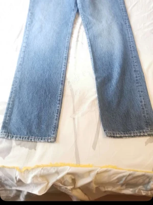 Blå raka jeans i klassisk modell - Säljer ett par blå jeans med rak passform och hög midja. Jeansen har en klassisk tvätt och är tillverkade i denim, vilket ger en tidlös look. Perfekta för dig som gillar enkel och stilren stil.