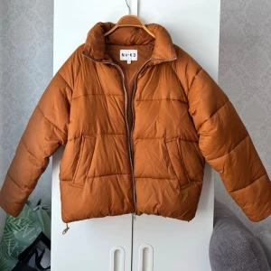 Orange pufferjacka - Orange pufferjacka från NA-KD med hög krage och dragkedja framtill. Jackan har två stora fickor på sidorna och quiltad design. Strl 34 men skulle mer säga 36-38 till passformen då den är oversized. Färgen är inte lika orange irl. Defekter: se två sista bilderna!❤️