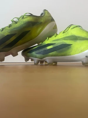 Adidas limegröna fotbollsskor - Säljer ett par snabba fotbollsskor från Adidas i limegrönt med svarta ränder på sidorna. Skorna har låg profil, snörning och en lätt ovandel i syntetmaterial. Sulan är vit med fasta dobbar, perfekt för spel på gräsplan. ADIDAS CRAZYFAST X