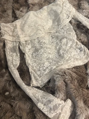 Vit off shoulder spetsblus - Säljer en superfin vit off shoulder blus i genomskinlig spets med blommönster. Tröjan har långa ärmar och volangdetalj upptill som ger en romantisk vibe. Perfekt att styla med jeans eller kjol för en trendig look.