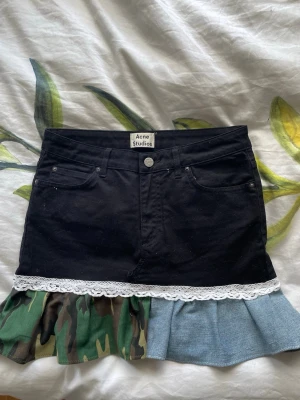 Svart kjol med volang från Acne Studios - Unik svart kortkjol från Acne Studios med volangkant i denim och camouflage samt vit spetsdetalj. Om du har funderingar om kjolen är det bara att du kontaktar! Priset går självklart att diskutera💝 (Gå in på min vinted Irene10rs för att läsa mina recensioner)