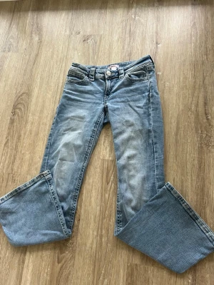 Ljusblå bootcut jeans med detaljer - Säljer ett par ljusblå bootcut jeans med snygga kontrastsömmar och broderade bakfickor. Jeansen har klassisk femficksmodell och låg midja. Perfekta för dig som gillar en avslappnad men trendig stil.