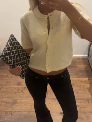 Kort gul kofta med pärlknappar - Söt kortärmad kofta i mjukt, fluffigt material och gul färg. Koftan har rund halsringning och pärlknappar framtill. Perfekt att styla med höga jeans eller kjol för en trendig look.
